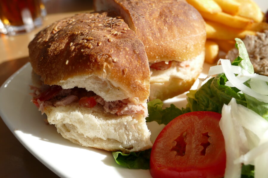 Halved Ftira sandwich with pulled pork, tomato salad and fries.
