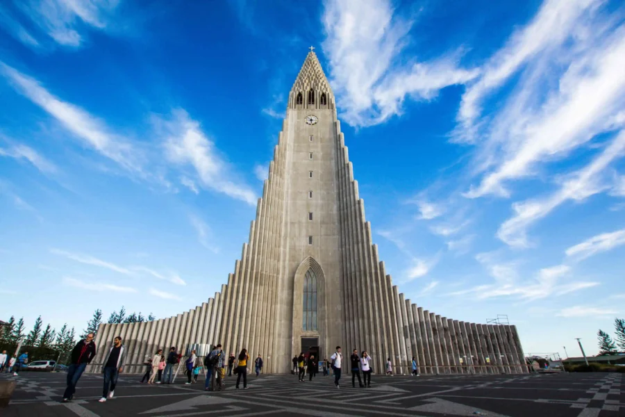 Hallgrímskirkja church, Reykjavík: Iconic basalt-inspired architecture against blue skies, with visitors exploring.