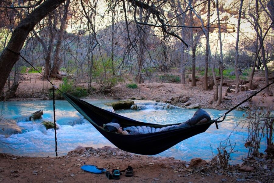 Relaxing in a black hammock by turquoise river among trees, embraced by natures tranquility.