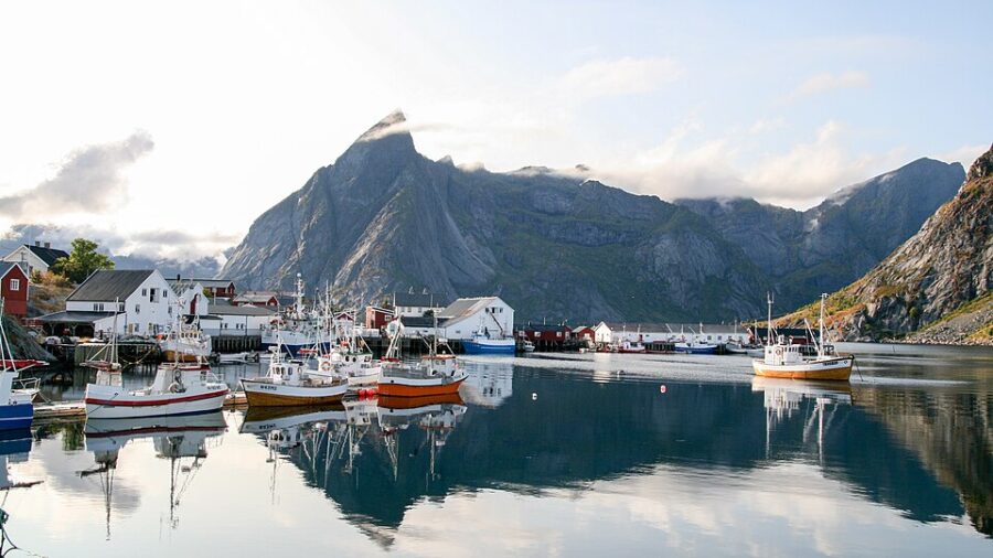 Boats are docked in Hamnøy Harbor, Norway, with majestic mountains rising in the background.