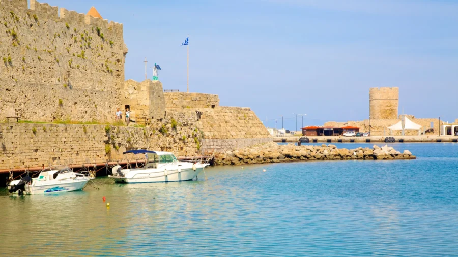 Rhodes harbor with medieval fortress, moored boats and Greek flag on Mediterranean.