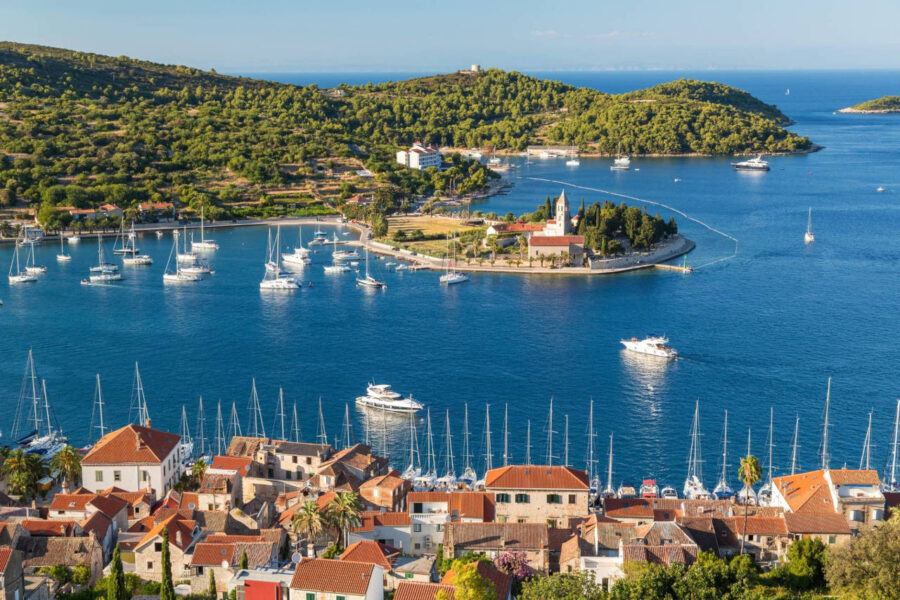 Mediterranean harbor town with terracotta roofs, marina of sailboats and church-topped promontory.