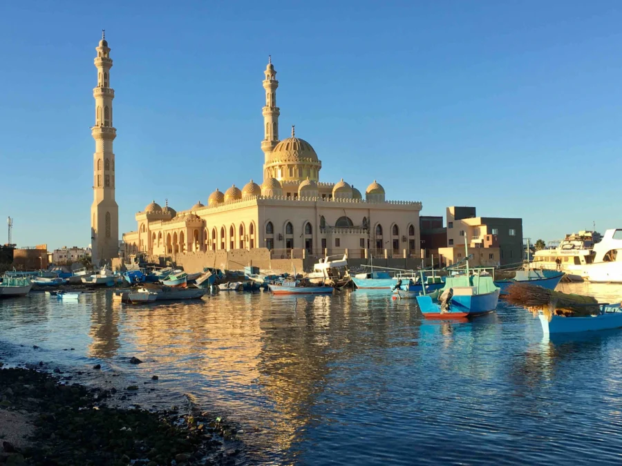 Waterfront mosque in Sakkala at sunset with fishing boats in calm harbor, Egypt travel scene.