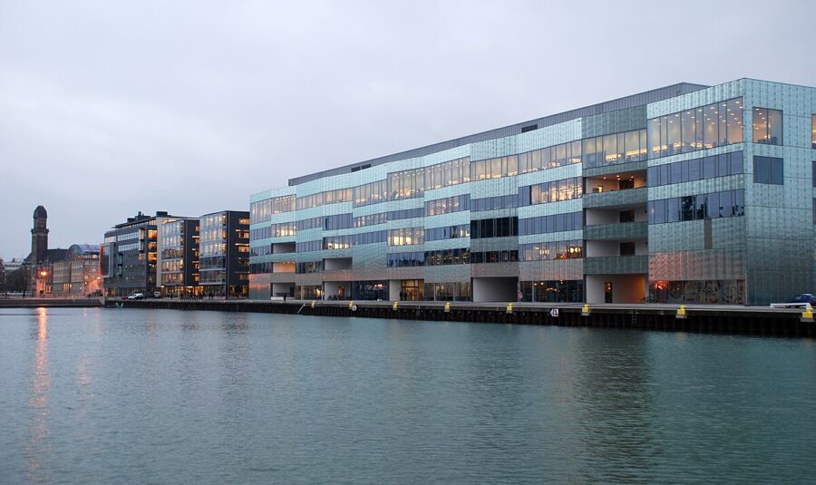 Malmö University waterfront office building with glass facade reflecting harbor at evening.