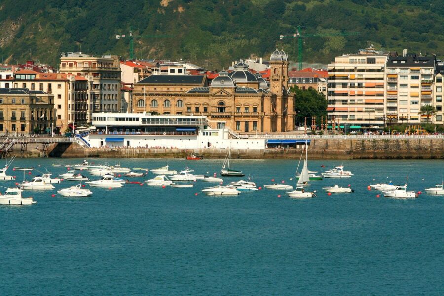 A vibrant harbor scene with sailboats, historic architecture, and lush green hills.