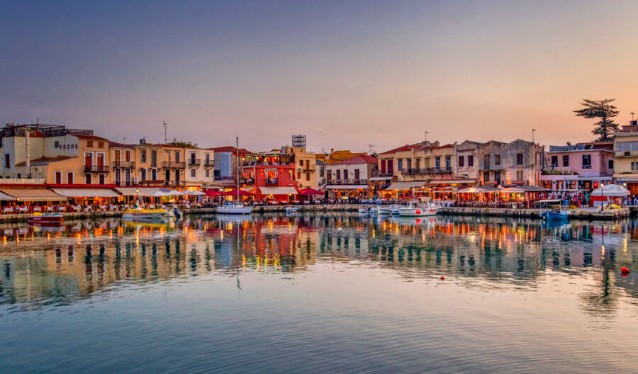 Twilight harbor scene with colorful buildings, boats, and reflections under a vibrant sky.