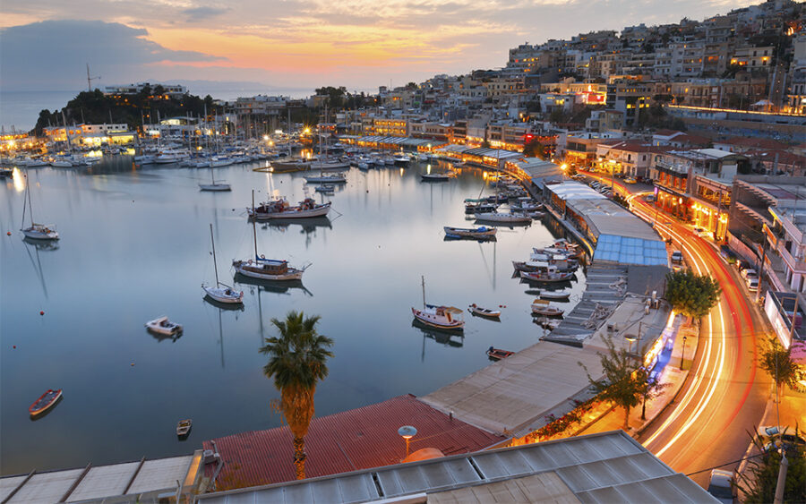 Twilight harbor scene with boats, buildings, palm tree, and vibrant sunset reflecting on water.