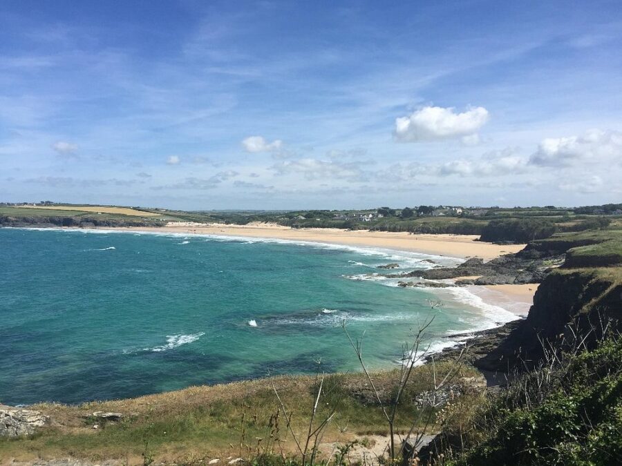 Scenic view of Harlyn Bay Beach and the ocean from a hilltop in Cornwall, England, showcasing sandy shores and waves.
