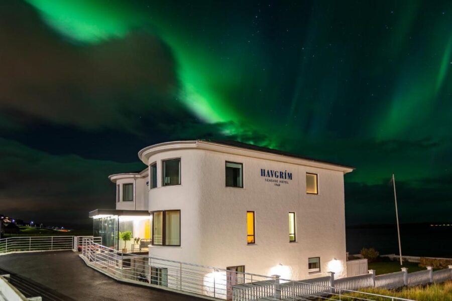 The northern lights shine over the Havgrim Seaside Hotel, 1948, set against the night sky in the Faroe Islands.