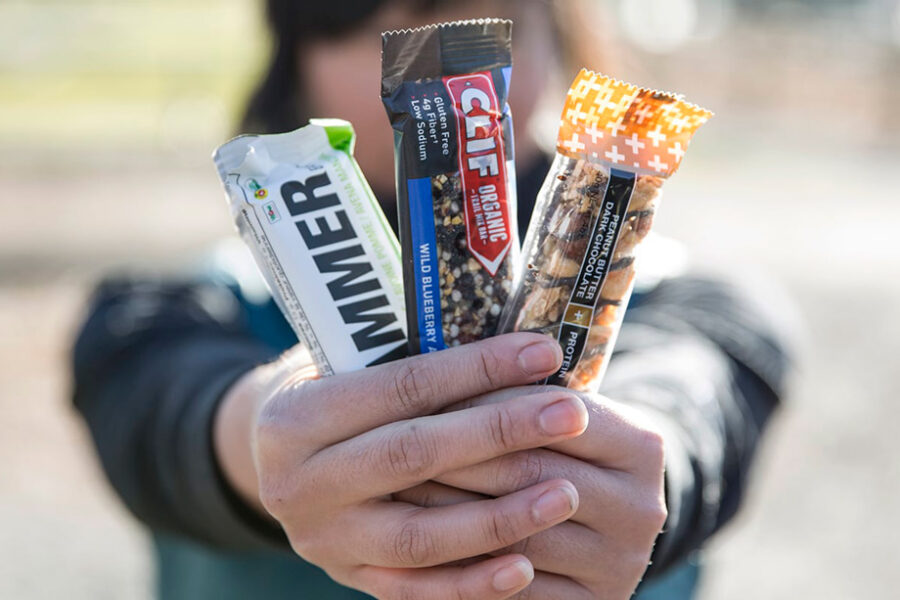 Hand holding energy bars outdoors: Hammer, Clif, and protein bar for active lifestyle.