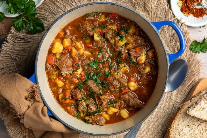 Hearty beef stew with vegetables and herbs in a rustic setting.