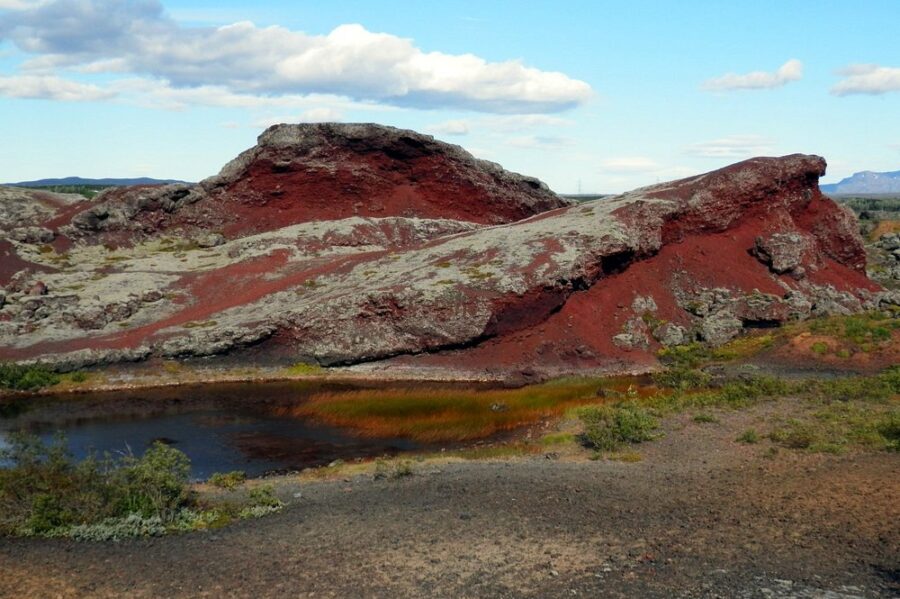 Striking red rock formation surrounds a tranquil pond in Heidmörk Nature Reserve.