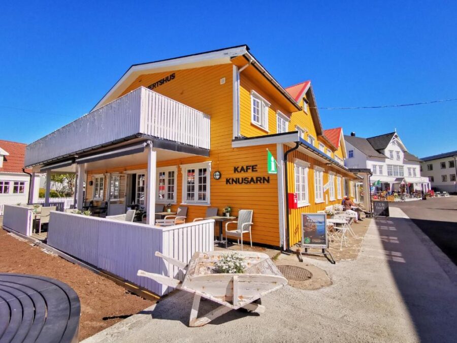 Henningsvær Guesthouse, a yellow building with a white fence and a bench, set in scenic Norway.