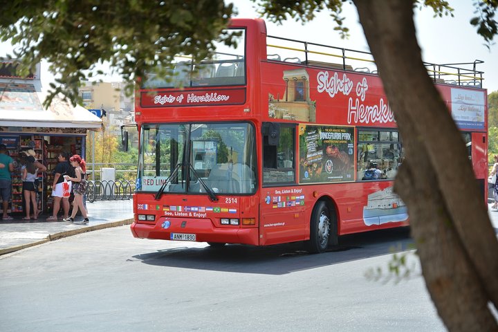 Sightseeing bus in Heraklion, Crete, explores vibrant, sunny tourist street scene.