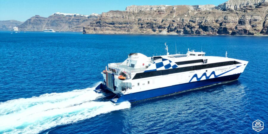 Sleek modern passenger ferry in clear blue sea with stunning cliffs in the background.