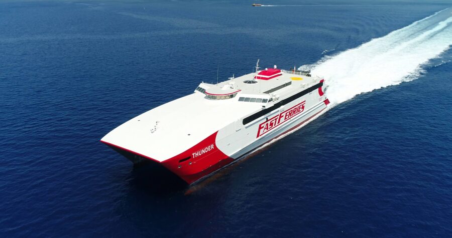 High-speed ferry catamaran Thunder in red and white slicing deep blue sea, aerial view.