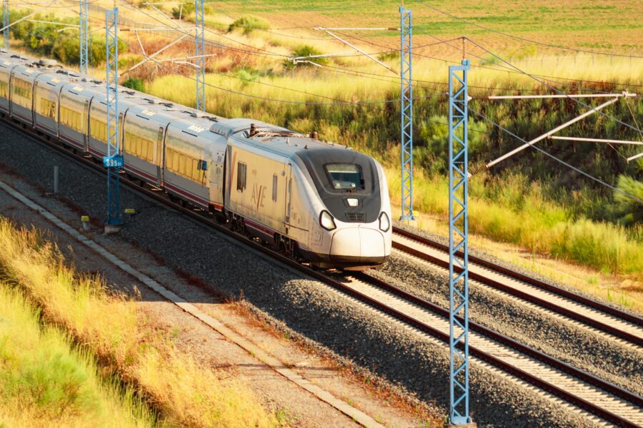 High-speed AVE train gliding through scenic landscape under sunlit skies.