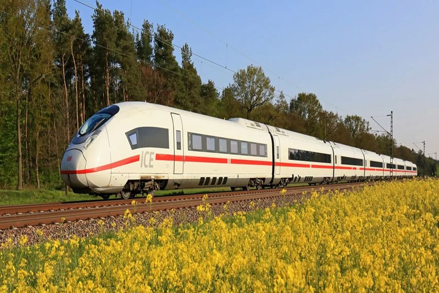 ICE high-speed train in motion against lush landscapes with yellow flowers and clear blue sky.