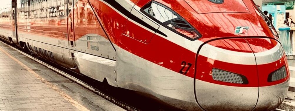 Red high-speed train at urban platform, sleek design, modern rail technology, passengers boarding.