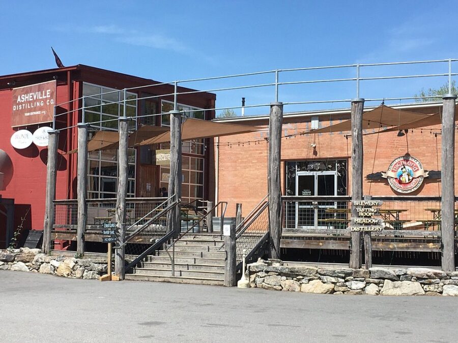 Front view of Highland Brewing Company, featuring a large red building with inviting entrance and outdoor seating.