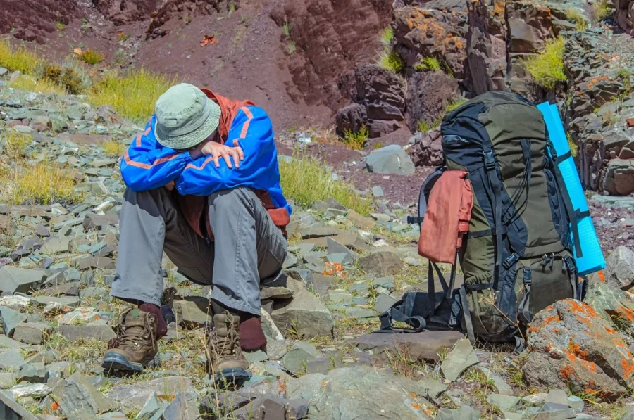 Hiker resting on rocky terrain with backpack in scenic mountain landscape.
