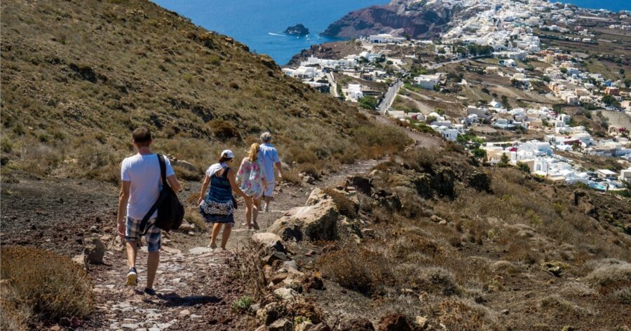 Hikers enjoy Santorinis scenic trail with coastal views, whitewashed architecture, and rugged terrain.