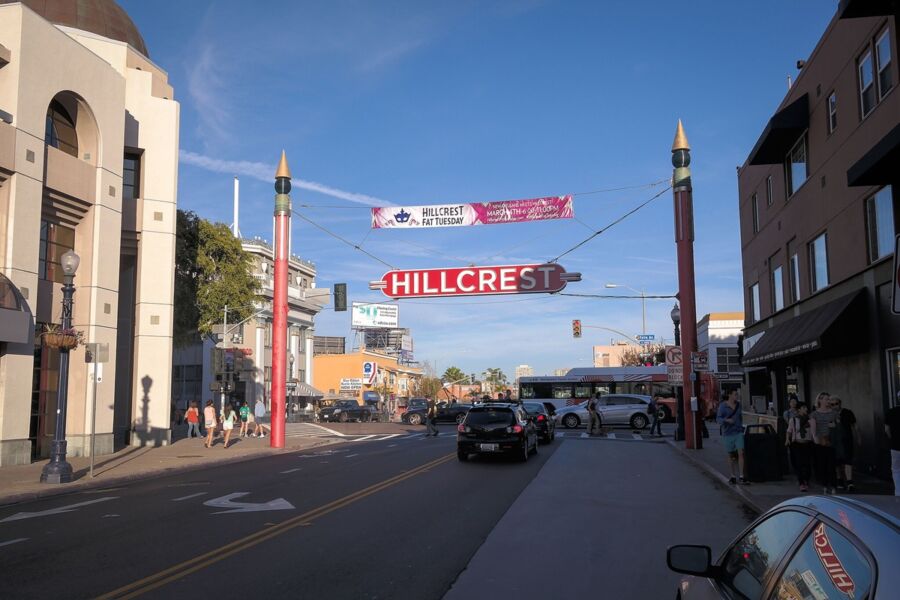 Vibrant Hillcrest street scene with sign, pedestrians, vehicles, and diverse architecture.