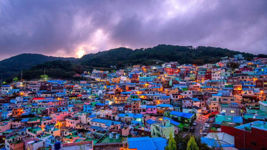 Colorful hillside neighborhood at dusk with vibrant homes and lush green hills.