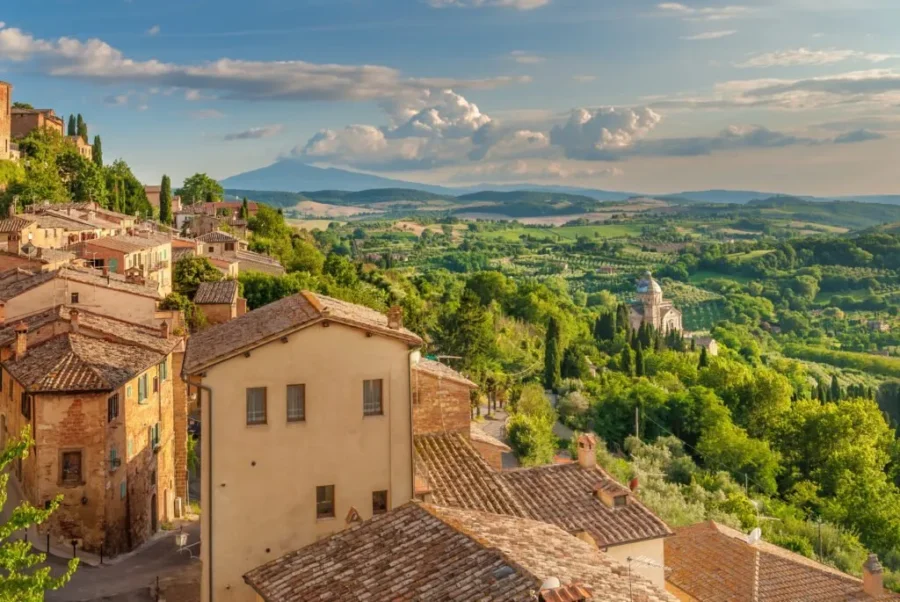 Hilltop Tuscan village overlooking green valley, vineyards and countryside church at golden hour.