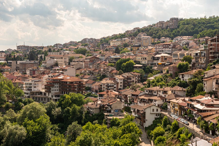 Veliko Tarnovo hillside panorama with red-tiled roofs, historic houses, greenery, and terraced streets.