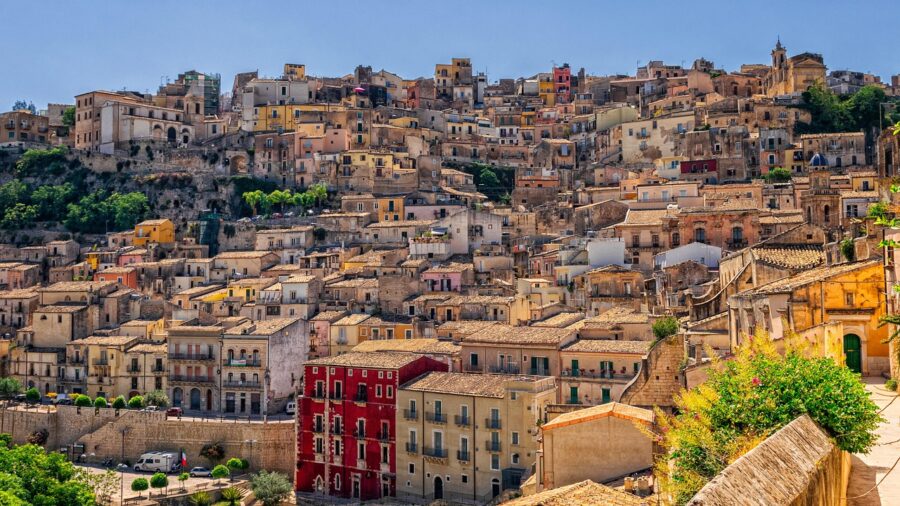 Charming Mediterranean hillside town with colorful buildings and lush greenery under a clear blue sky.