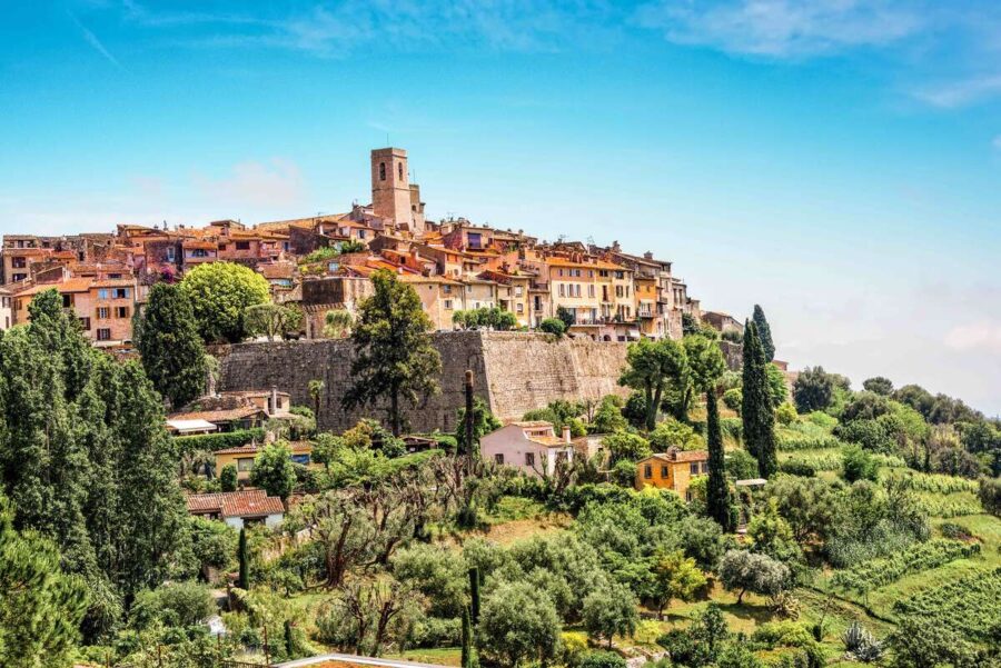 Hilltop village with terracotta roofs and lush greenery under a vibrant blue sky.