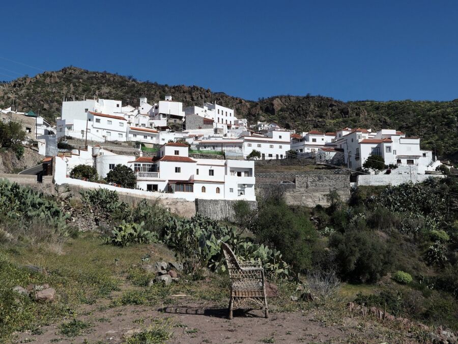 Picturesque Tejeda hillside village with whitewashed houses, red-tiled roofs, wicker chair, and lush vegetation.