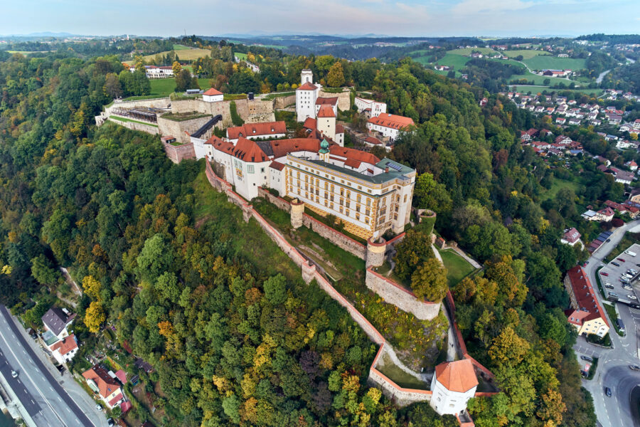 Aerial view of Veste Oberhaus hilltop fortress and medieval castle atop wooded ridge.