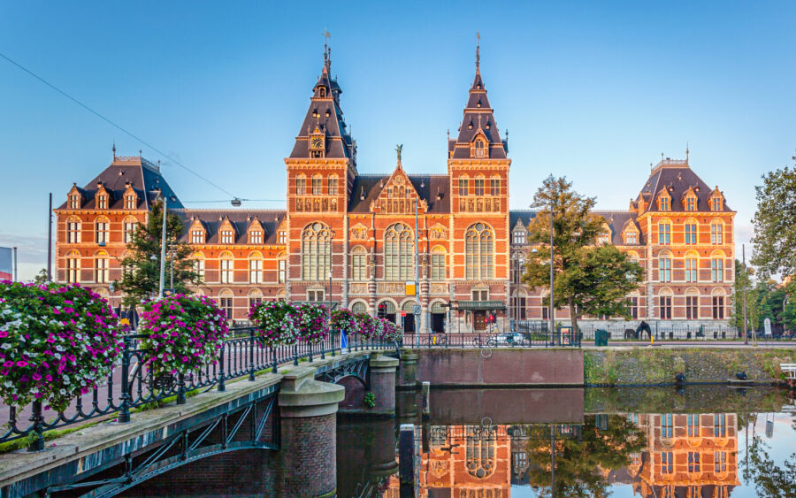 Majestic red brick Rijksmuseum with spires over canal, reflecting urban history and architecture.