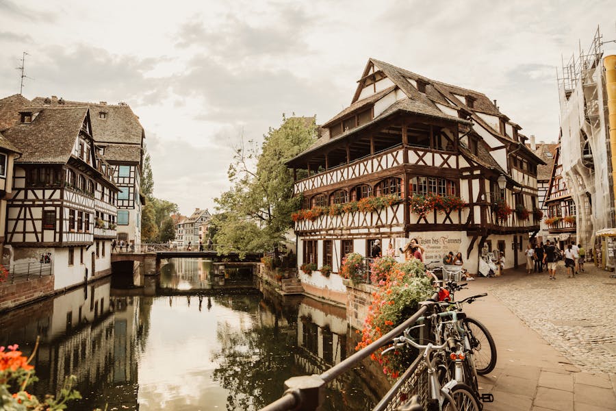 Historic Strasbourg canal with half-timbered house, stone bridge, bicycles, and flower-filled balconies.