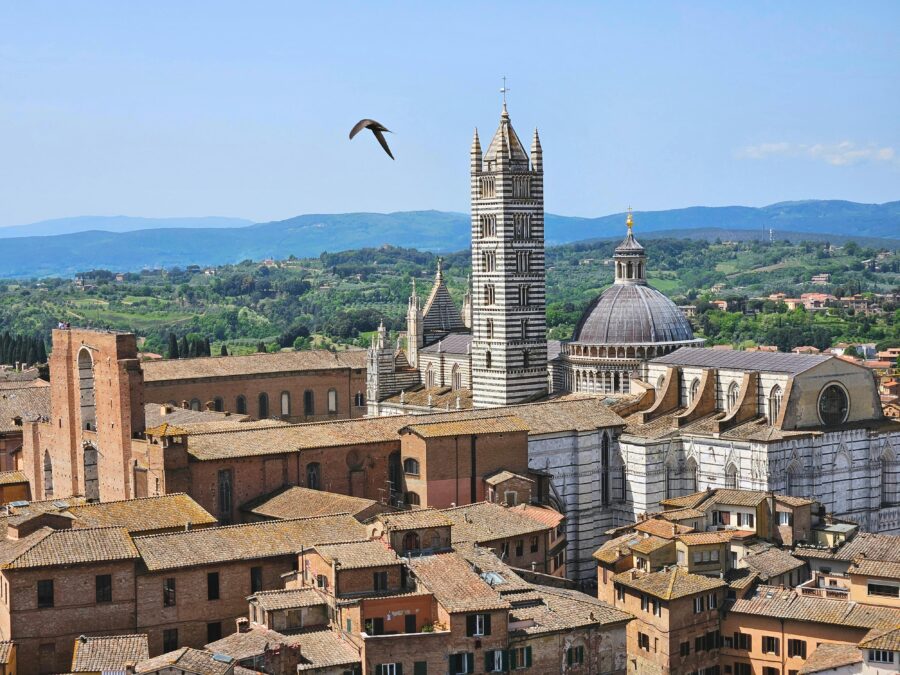 Aerial view of Siena Duomo cathedral with terracotta roofs in historic Tuscan cityscape.