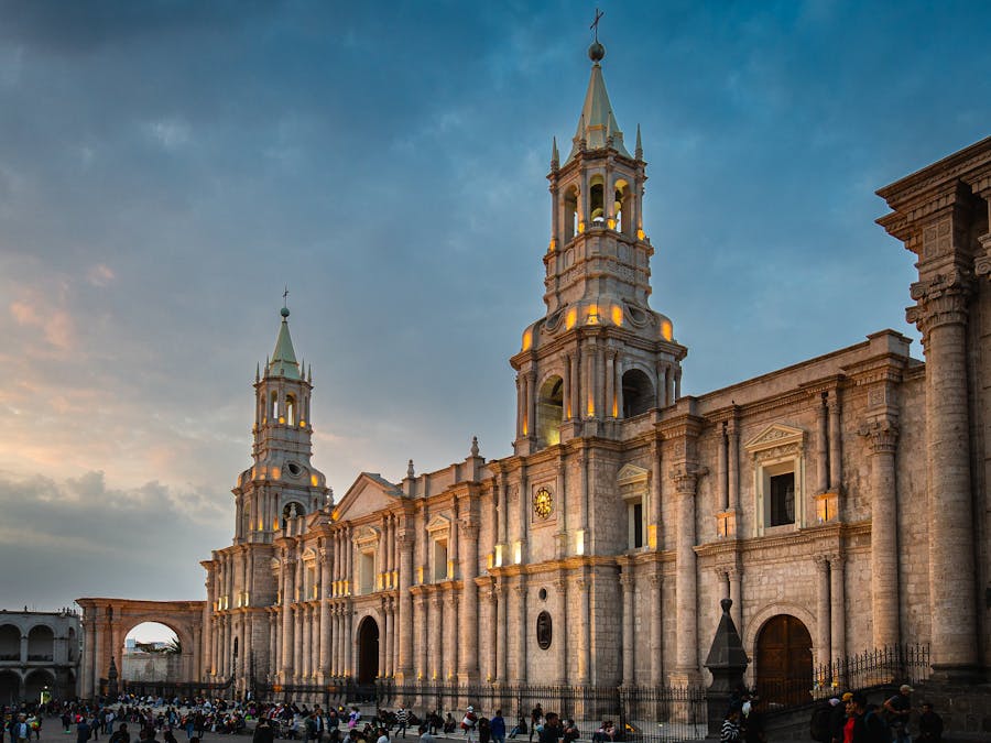 Historic baroque cathedral illuminated at dusk overlooking busy city plaza with tourists and locals.