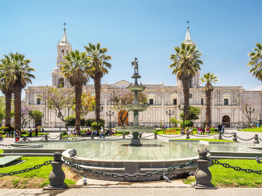Historic Plaza de Armas cathedral with fountain, palm trees, and people in sunny city square.