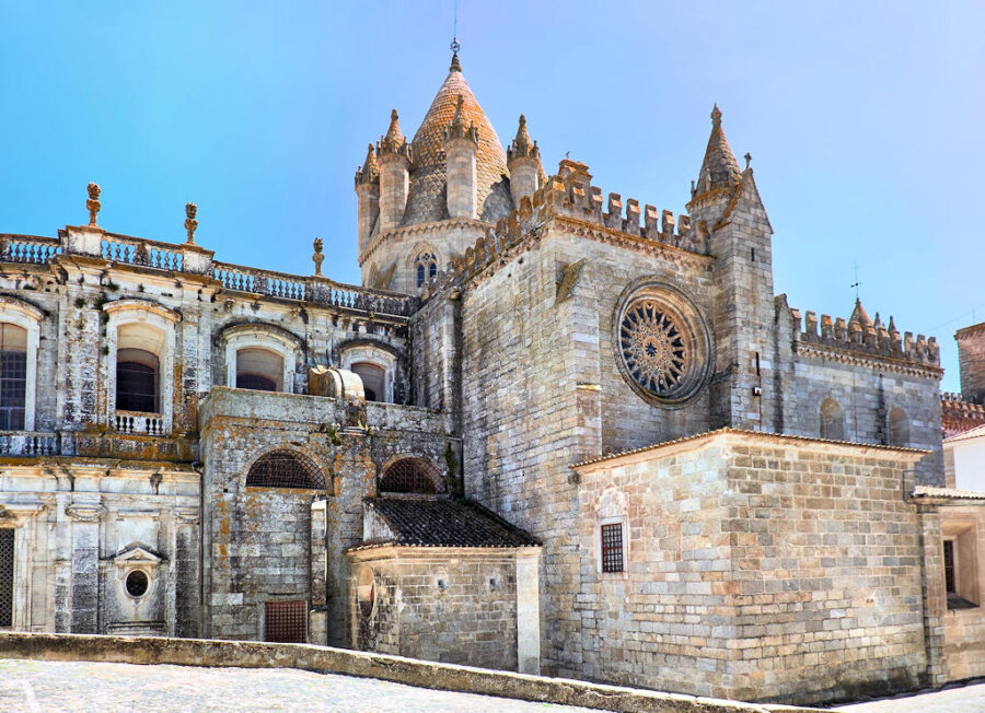 Gothic-Romanesque cathedral with rose window, spires, and stone façade under blue sky.