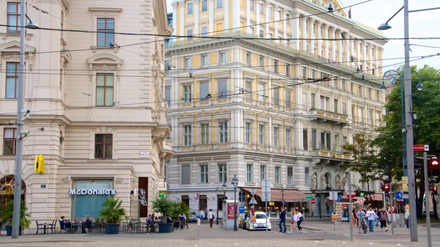 Vienna historic city corner with McDonalds, ornate buildings, tram wires, and pedestrians.