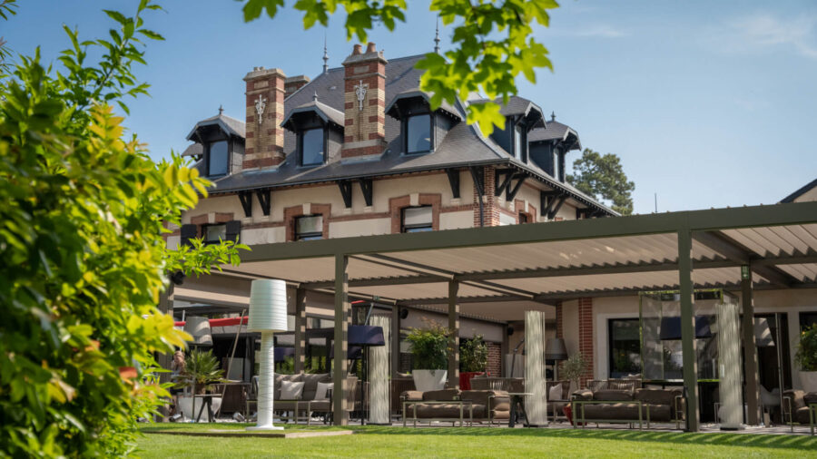 Historic French mansion with modern pergola terrace and garden lawn, luxury hotel outdoor lounge.