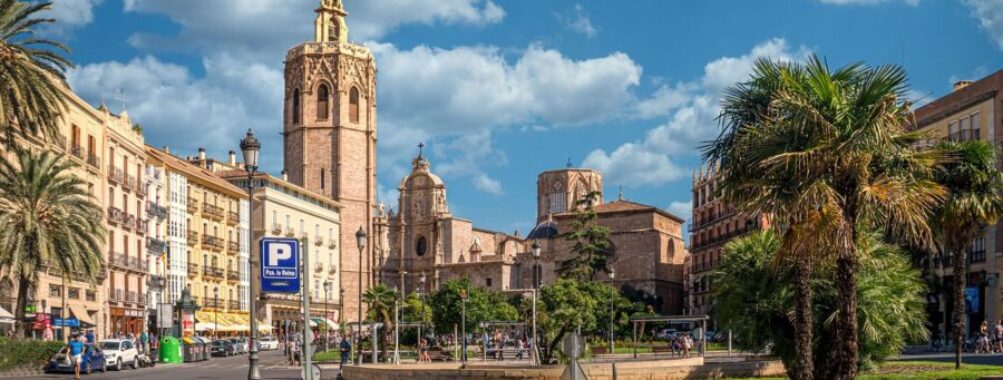Vibrant Mediterranean city square with historical architecture, palm trees, and bustling street life.