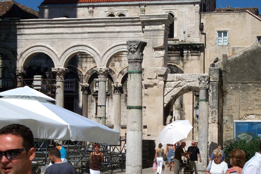 Ancient stone structure with arches, modern visitors, sunny day, historical site, preservation efforts.