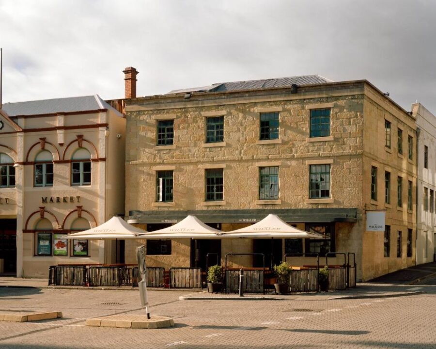 Historic sandstone hotel and market building with outdoor café seating on a quiet cobblestone street.