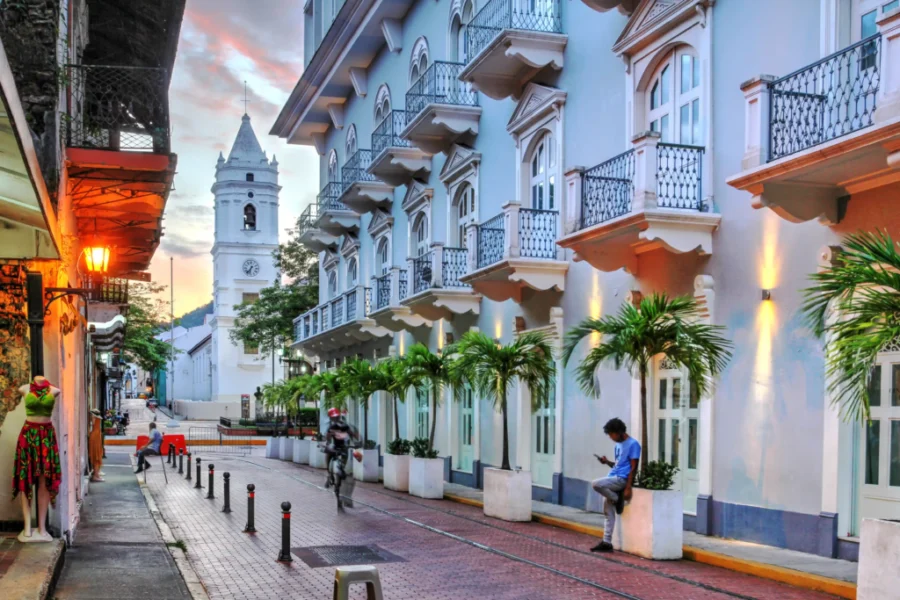 Charming urban street with historical architecture, cultural storefronts, and a clock tower at sunset.