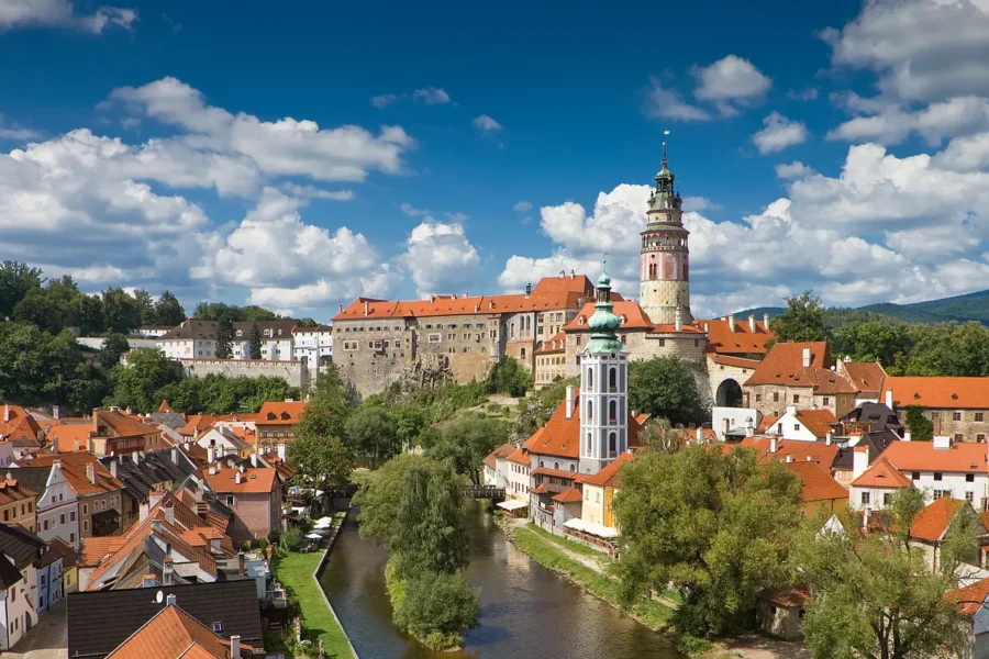 Charming Český Krumlov town river view with castle and clock tower amidst rolling hills.