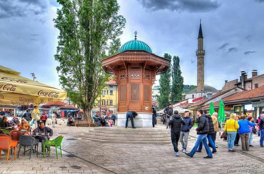 Sebilj Fountain in Sarajevo’s Baščaršija square with Ottoman architecture, mosque minaret, and cafés.