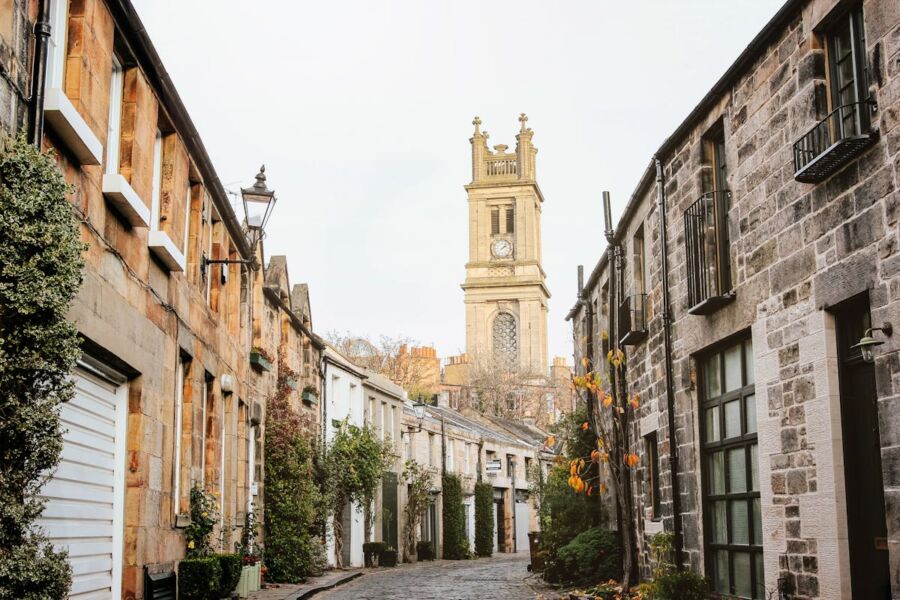 Narrow cobblestone street with historical stone buildings and prominent clock tower in autumn.