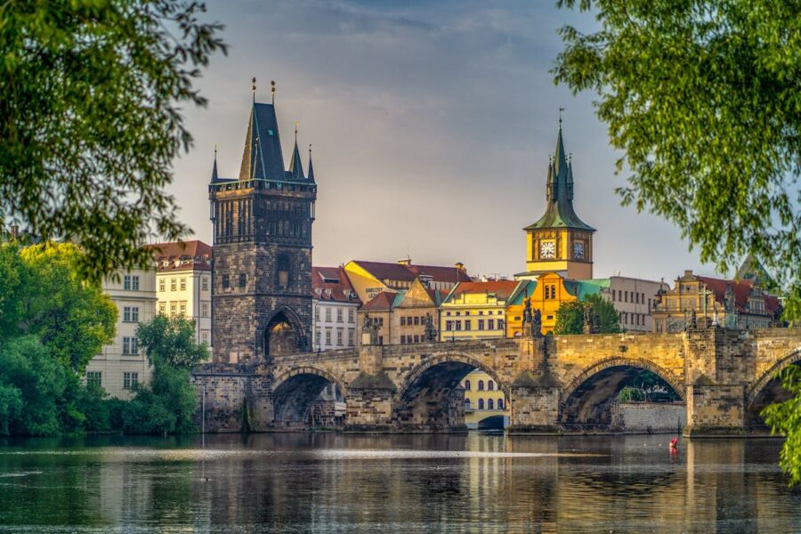 Scenic Charles Bridge with reflections, Gothic tower, clock tower, trees, and kayak in Prague.